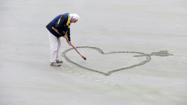 An old man writing a heart on the ground
